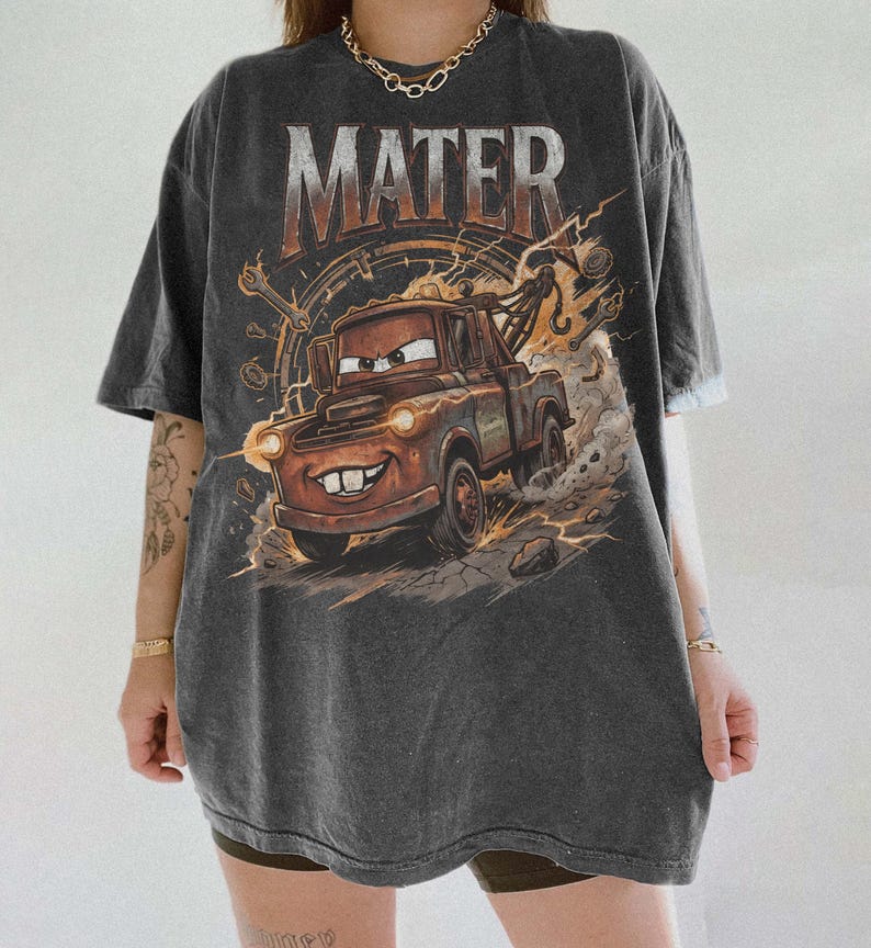 May include: A charcoal gray short-sleeve t-shirt featuring a large graphic print of the character Mater from the movie Cars. The design includes the text MATER in bold letters above the rusty tow truck, surrounded by wrenches and dust clouds.