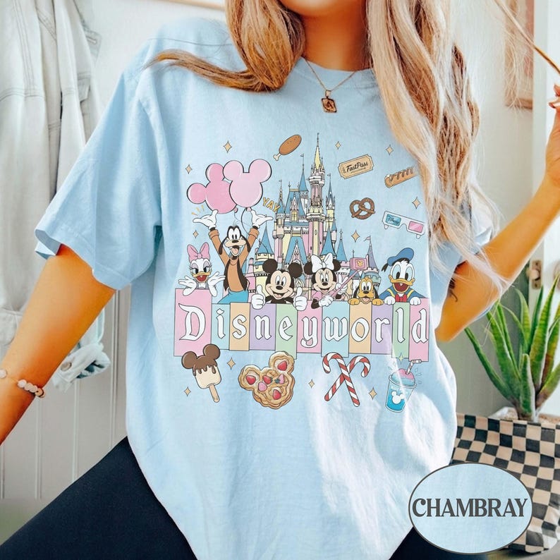 May include: Pale blue t-shirt with a Disney World graphic. The design features Mickey and Minnie Mouse, Goofy, Donald Duck, and other characters, along with the Disney World castle and food icons. The word "Disneyworld" is written across the bottom of the design.