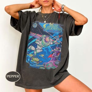 Puede incluir: Camiseta gris oscuro con un gr&aacute;fico colorido de Buzz Lightyear en el espacio, con el texto "Buzz Lightyear Laser Blast" y "Discoveryland". El dise&ntilde;o incluye extraterrestres y Zurg. La camiseta tiene mangas cortas y un corte relajado.