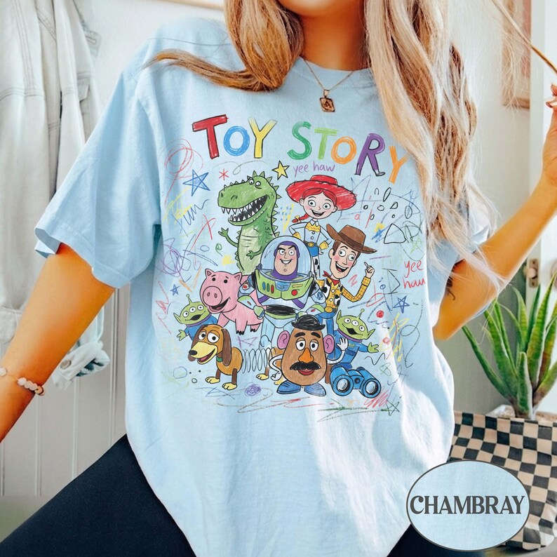 Pode incluir: T-shirt azul claro com um gr&aacute;fico colorido dos personagens de Toy Story, incluindo Woody, Buzz Lightyear e Rex. As palavras "Toy Story" s&atilde;o escritas em uma fonte l&uacute;dica e colorida. A camisa tem mangas curtas e um ajuste relaxado.