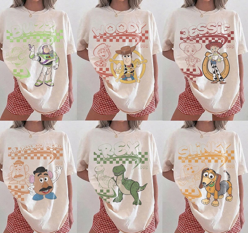 May include: A collection of six off-white t-shirts featuring Toy Story characters including Buzz Lightyear, Woody, Jessie, Mr. Potato Head, Rex, and Slinky. Each shirt displays a retro-style graphic with a checkered pattern and the character name.