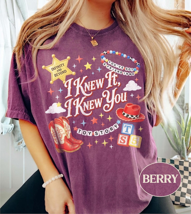 May include: A berry-colored t-shirt featuring a graphic print with the text I KNEW IT, I KNEW YOU, TOY STORY, INFINITY AND BEYOND, and YOU'VE GOT A FRIEND IN ME. The design includes a yellow sheriff star, red cowboy boots, a red hat, and alphabet blocks.