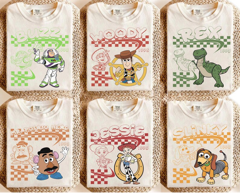 May include: Six off-white t-shirts featuring Toy Story characters: Buzz Lightyear, Woody, Rex, Mr. Potato Head, Jessie, and Slinky Dog. Each shirt displays the character name, a checkered pattern, the year 1995, and a line-art sketch of the character.