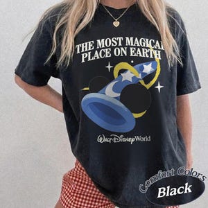 Puede incluir: Camiseta negra con el texto "THE MOST MAGICAL PLACE ON EARTH" y un gr&aacute;fico de un sombrero de mago azul con estrellas y orejas de Mickey Mouse. La camiseta tambi&eacute;n tiene las palabras "Walt Disney World" impresas debajo.