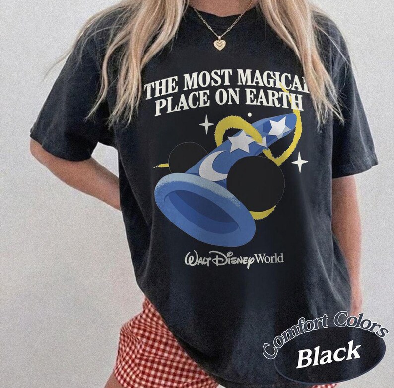 Puede incluir: Camiseta negra con el texto "THE MOST MAGICAL PLACE ON EARTH" y un gr&aacute;fico de un sombrero de mago azul con estrellas y orejas de Mickey Mouse. La camiseta tambi&eacute;n tiene las palabras "Walt Disney World" impresas debajo.