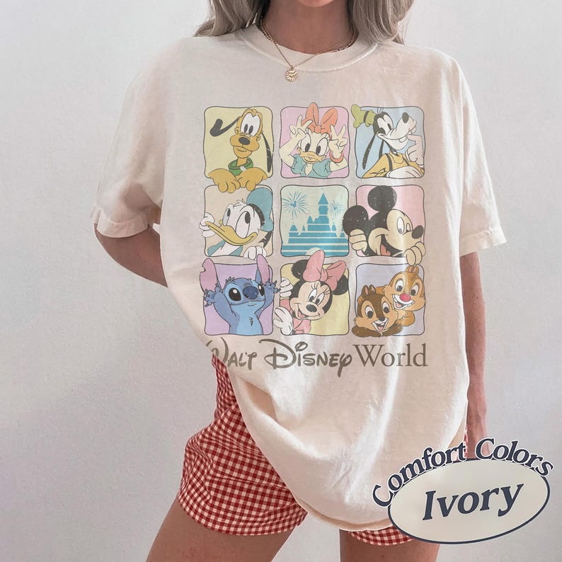 May include: Ivory-colored t-shirt featuring a grid of Disney characters including Mickey Mouse, Donald Duck, and Stitch. The words "Walt Disney World" are printed below the grid. The shirt is a Comfort Colors brand.