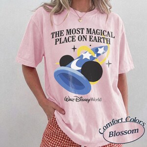 Puede incluir: Camiseta rosa claro con el texto "THE MOST MAGICAL PLACE ON EARTH" y un gr&aacute;fico de un sombrero de mago azul y negro con estrellas. Las palabras "Walt Disney World" est&aacute;n impresas debajo.