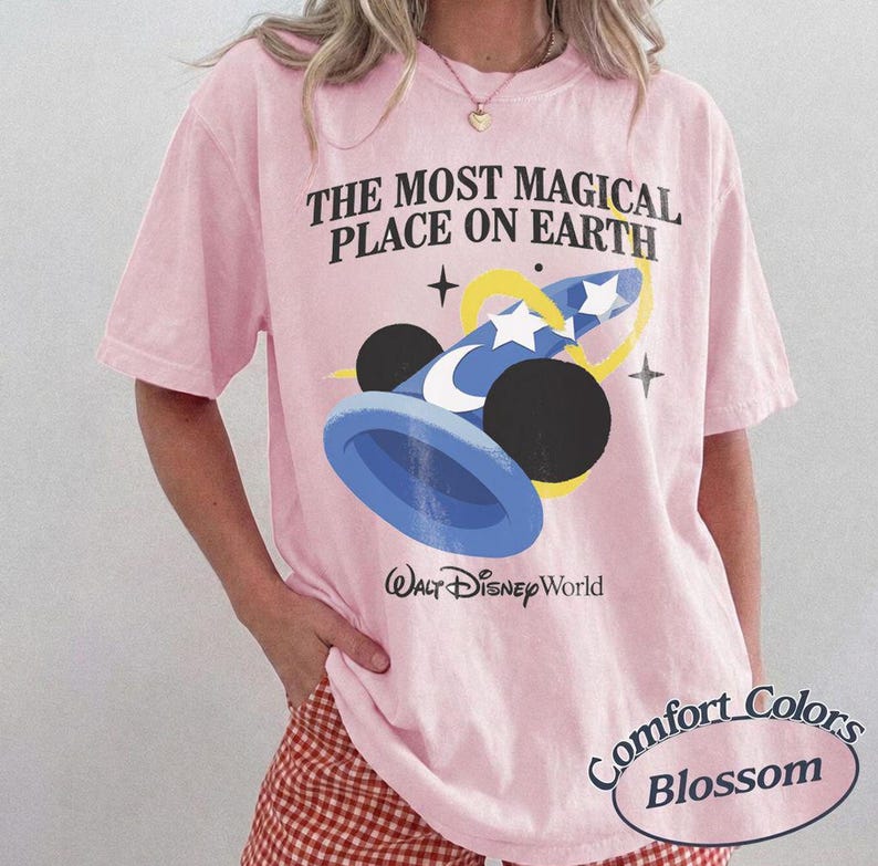 Puede incluir: Camiseta rosa claro con el texto "THE MOST MAGICAL PLACE ON EARTH" y un gr&aacute;fico de un sombrero de mago azul y negro con estrellas. Las palabras "Walt Disney World" est&aacute;n impresas debajo.