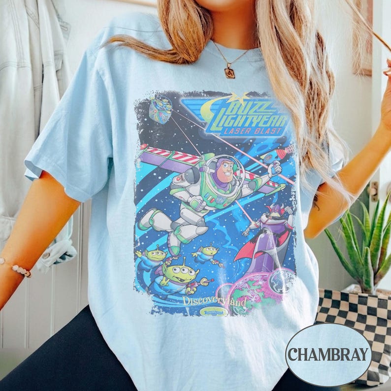 Puede incluir: Camiseta azul claro con un gr&aacute;fico colorido de Buzz Lightyear en el espacio, con el texto "Buzz Lightyear Laser Blast" y "Discoveryland". El dise&ntilde;o incluye extraterrestres y el villano Zurg. La camiseta es de material suave.