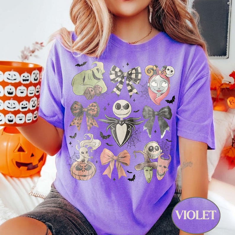 May include: A purple t-shirt featuring a graphic print of various characters and bows from The Nightmare Before Christmas, including Jack Skellington, Sally, Oogie Boogie, Zero, and Lock, Shock, and Barrel, arranged with spiderwebs and bats.