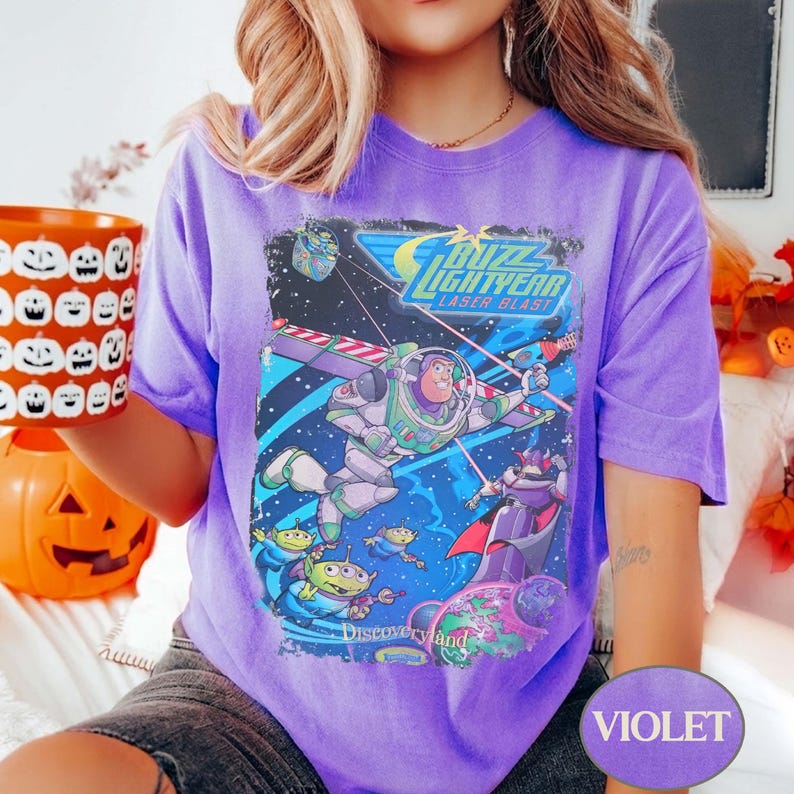 Puede incluir: Una camiseta violeta con un gr&aacute;fico de Buzz Lightyear Laser Blast. El dise&ntilde;o incluye a Buzz Lightyear con un traje espacial, extraterrestres y el texto "Discoveryland". La camiseta es de color violeta liso.
