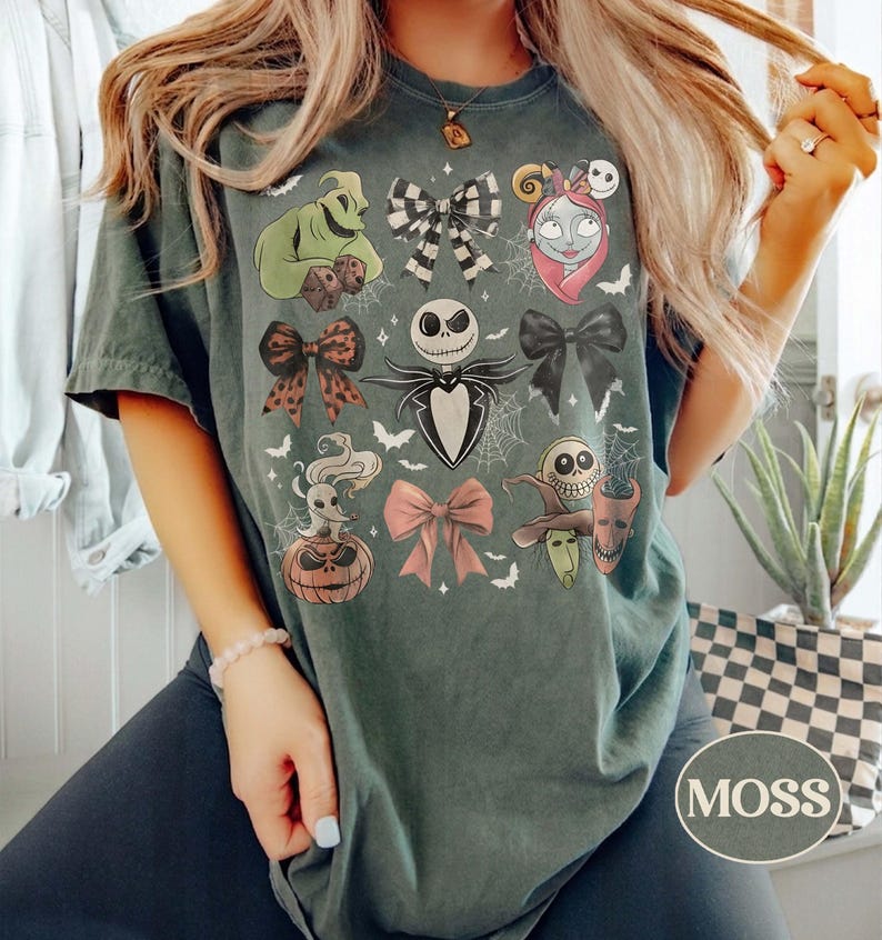 May include: A dark green t-shirt featuring a graphic print of characters and bows from The Nightmare Before Christmas. The design includes Jack Skellington, Sally, Oogie Boogie, Zero, and various bows arranged in a grid pattern with spiderwebs.