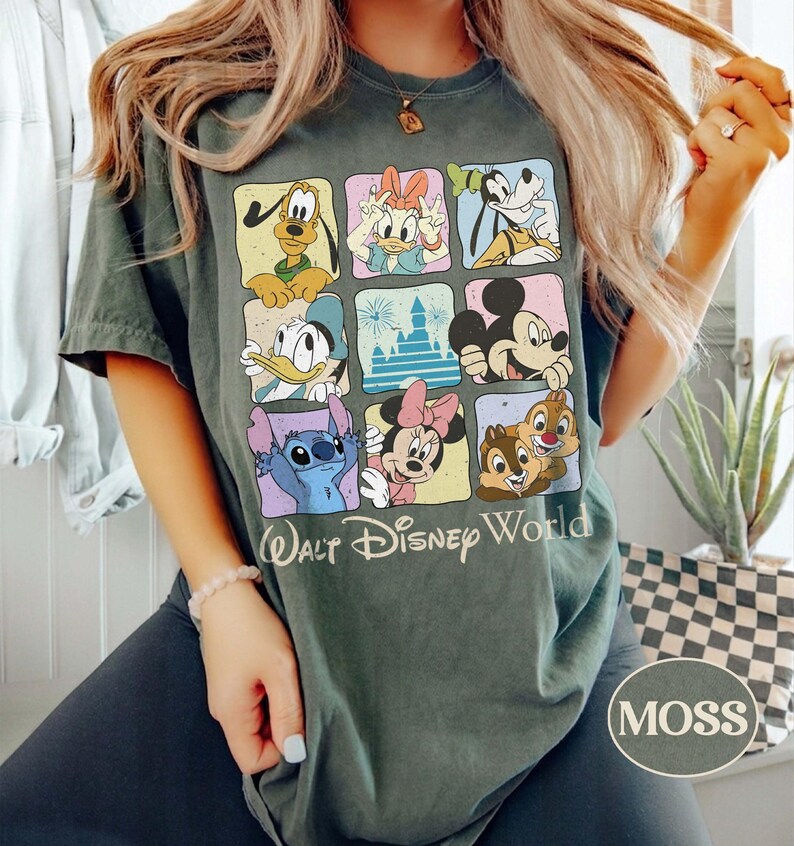 May include: Moss green t-shirt featuring a grid of Disney characters including Mickey Mouse, Donald Duck, and Stitch. The words "Walt Disney World" are printed below the grid. The shirt has a crew neck and short sleeves.