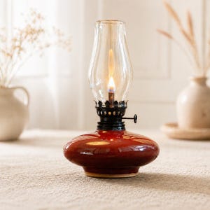 May include: A vintage-style oil lamp with a clear glass chimney and a bright flame. The lamp has a glossy, deep red base and a black metal frame. It is a decorative item, perfect for adding a warm, inviting glow to any space.