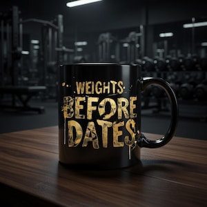 May include: Black ceramic mug with the text "WEIGHTS BEFORE DATES" in gold lettering. The mug has a black handle and is sitting on a wooden surface. The background is a blurred gym setting.