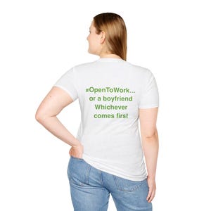 May include: A white short-sleeved t-shirt featuring green text on the back that reads #OpenToWork... or a boyfriend Whichever comes first. The shirt is paired with blue denim jeans, showing a casual style with a clear, legible message printed.