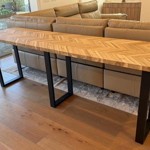 May include: A long, rectangular wooden console table with a herringbone pattern top. The table has black metal legs. The table is approximately 60 inches long, 15 inches wide, and 30 inches tall.