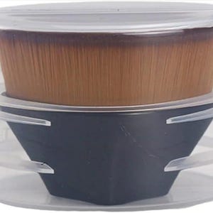 May include: A makeup brush with a black base and a clear plastic case. The brush head is a light brown color. The case has a clear lid and a clear base with a black, angled holder for the brush.