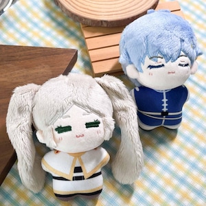 May include: Two plush dolls with embroidered facial features. One doll has light blue hair and a blue outfit with white accents. The other doll has long white hair in pigtails, green embroidered eyes, and a white outfit with gold and black details.