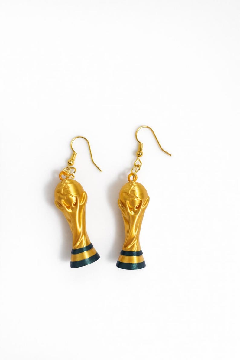 May include: A pair of gold-colored trophy earrings with a dark blue and green stripe at the base. The earrings are suspended from gold-colored ear wires, set against a white background.