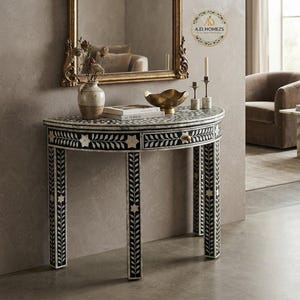 May include: A semi-circular console table featuring intricate black and white floral inlay patterns across its surface and four legs. The table includes a single central drawer with a small knob and a curved top edge, showcasing detailed craftsmanship.