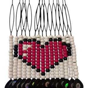 May include: A beaded hair accessory with a black base and black wire attachments. The beads are white, black, and pink. The accessory has a series of black teardrop-shaped charms at the bottom, each with a number.