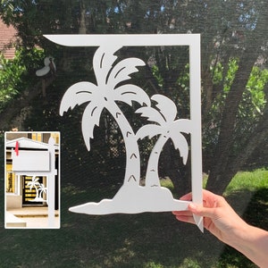 Op de afbeelding: Witte metalen brievenbuspaaltopper met een uitgesneden ontwerp van twee palmbomen. De topper wordt getoond tegen een groene achtergrond.