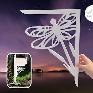 Op de afbeelding: Witte houten brievenbusbeugel met een libellenontwerp. De beugel is uitgesneden in de vorm van een libel met ingewikkelde details. De beugel wordt getoond tegen een nachtelijke hemel met sterren.