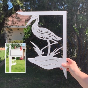 Op de afbeelding: Witte houten uitsnijding van een reiger die in een moeras staat. De uitsnijding is ontworpen om te worden gebruikt als een brievenbuspaaltopper.