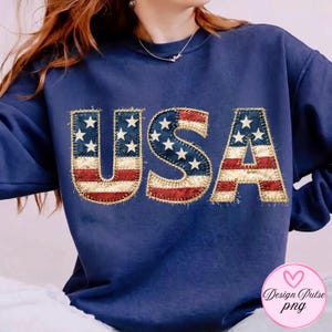 May include: Navy blue sweatshirt with the word "USA" in a patriotic design. The letters feature the American flag with red and white stripes and blue fields with white stars. The design has a stitched, textured appearance.