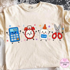 May include: A cream-colored t-shirt featuring a graphic print of four anthropomorphic school supplies: a blue calculator, a red alarm clock, a white glue bottle labeled GLUE, and red scissors, all surrounded by small colorful stars and hearts.