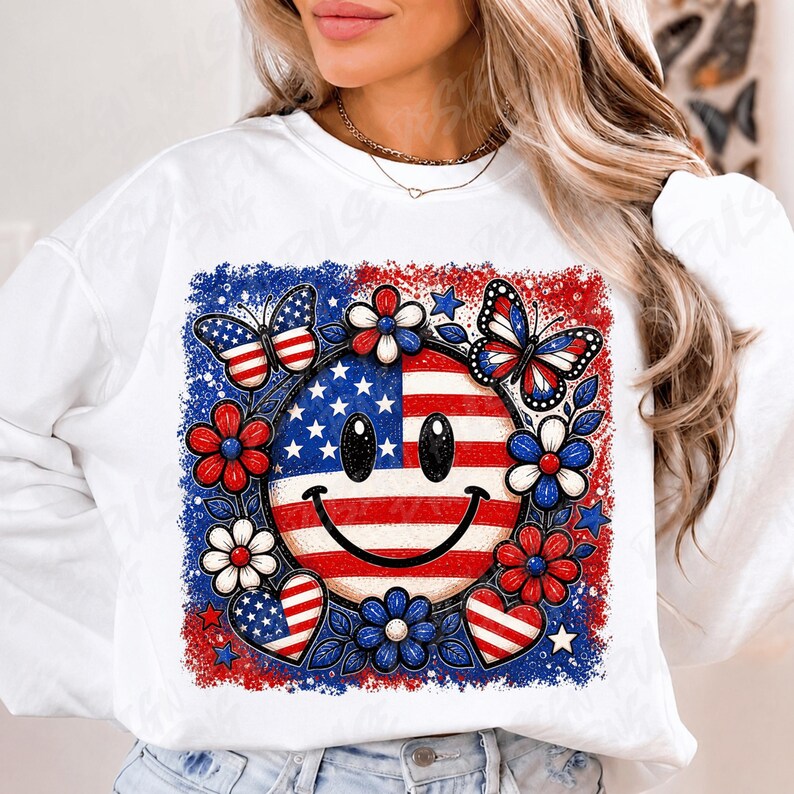 May include: White sweatshirt featuring a patriotic design. The graphic includes a smiley face with the American flag, surrounded by red, white, and blue flowers, butterflies, and hearts. The design has a distressed, vintage look.