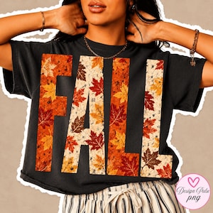 May include: A black short-sleeved t-shirt featuring the word FALL printed in large block letters. The letters are filled with a detailed pattern of autumn maple leaves in shades of orange, red, yellow, and brown against a light speckled background.