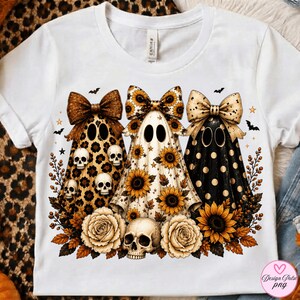 May include: A white t-shirt featuring a graphic of three ghosts wearing large bows. The ghosts have leopard print, sunflower, and polka dot patterns. The design includes sunflowers, roses, and skulls, with small bats and stars scattered around.