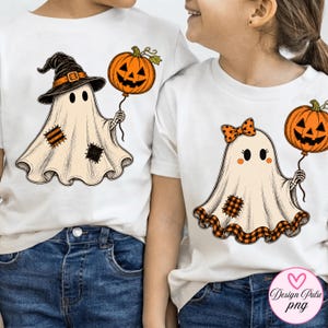 May include: Two white t-shirts featuring Halloween graphics. One shirt displays a ghost wearing a black witch hat and holding an orange jack-o'-lantern balloon. The other shirt shows a ghost with an orange plaid bow holding a jack-o'-lantern balloon.
