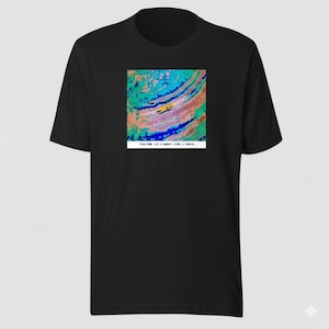 May include: Black t-shirt featuring a colorful abstract design in shades of blue, green, pink, and yellow. The design is a square shape. The text "TLB.COM - LAT -21.000777 - LONG -11.000732" is printed below the design.