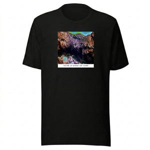 Könnte beinhalten: Schwarzes T-Shirt mit einem quadratischen Grafikdesign einer farbenfrohen Berglandschaft. Die Grafik zeigt Grün-, Braun-, Lila- und Blautöne. Der Text "TLR.COM - LAT: 40.234534 - LON: -73.972551" ist darunter gedruckt.