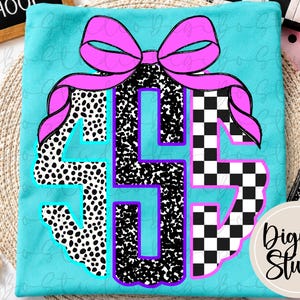 May include: A bright turquoise t-shirt featuring a large, centred monogram graphic. The letters are decorated with black and white patterns, including spots and a checkerboard design, topped with a vibrant pink bow with purple outlines.