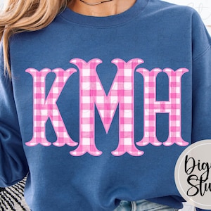 May include: A navy blue sweatshirt featuring the letters "KMH" in a pink and white gingham pattern. The letters have a decorative, scalloped edge. The lower right corner of the sweatshirt has a circular logo that reads "DigiBo Studio".