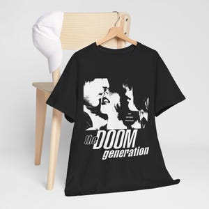 May include: A black short-sleeved t-shirt featuring a high-contrast white graphic of three faces in profile. The text "the DOOM generation" is printed in white below the graphic, with smaller text "REX. AMY. XAVIER. WHATEVER." visible to the right.