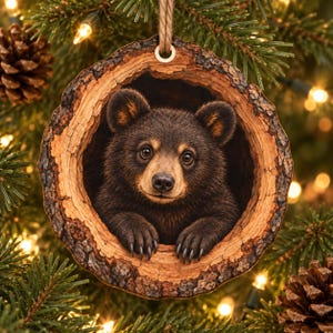 May include: A round, wood-slice Christmas ornament featuring a detailed illustration of a brown bear cub peering out from a hollow tree trunk. The ornament has a rough, textured bark edge and is suspended by a simple, light brown twine loop.