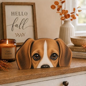 Puede incluir: Un recorte de madera con forma de cabeza de perro beagle con pelaje marrón y blanco, grandes ojos oscuros y orejas largas. El perro está representado con una mancha blanca en la frente y una nariz negra, creando un retrato realista.