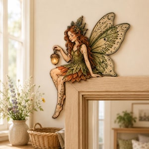 May include: A wall-mounted decorative figure of a fairy with long red hair, wearing a green leaf-patterned dress and large, detailed wings. The fairy holds a small, glowing acorn-shaped lantern and sits perched on the edge of a wooden frame.
