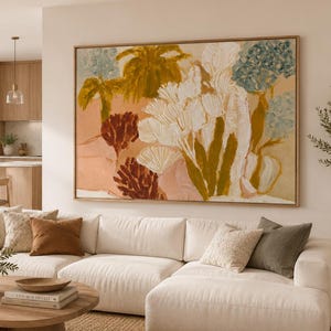 Puede incluir: Una gran pieza de arte mural rectangular enmarcada que presenta una pintura botánica abstracta con pinceladas gruesas y texturizadas en tonos blanco, amarillo mostaza, terracota y azul apagado, sobre una pared beige encima de un sofá blanco.