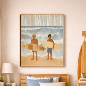 May include: A framed wall art print depicting two individuals standing on a sandy beach holding surfboards, with blue ocean waves in the background. The artwork features a colour palette of light blue, tan, and white, presented in a wooden frame.