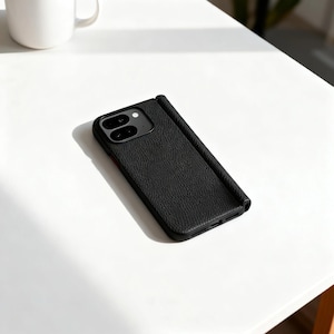 May include: Black textured leather phone case with a camera cutout and a fold-over cover. The case is designed to protect the phone and has a sleek, modern look. The case is shown on a white surface.
