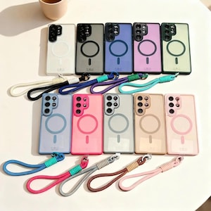 Puede incluir: Una colección de fundas de teléfono coloridas con correas de muñeca a juego. Las fundas son de varios colores, incluyendo blanco, gris, azul, rosa y verde. Cada funda tiene un diseño circular y una función magnética. Las correas de muñeca son de colores coordinados.