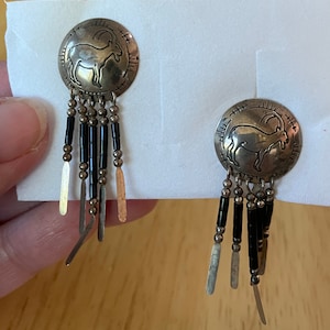 Puede incluir: Un par de pendientes colgantes de plata con cuentas negras y un dije de plata de una cabra de montaña.