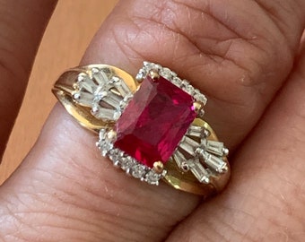 May include: A gold ring featuring a large, square-shaped red gemstone surrounded by smaller, clear gemstones.