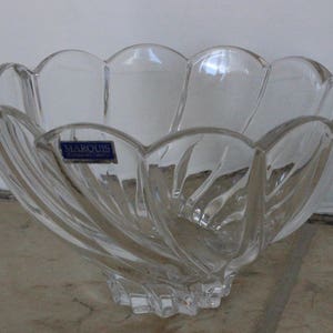 May include: A clear glass bowl with a scalloped rim and a swirl design. The bowl has a sticker on the side that says "Marquis Crystal of Austria".